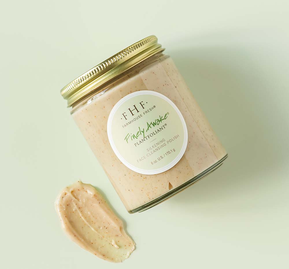 A jar and texture smudge of Finely Awake face polish on a green background.